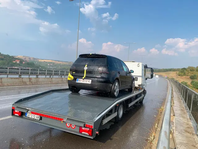 Crni Golf na platformi šlep vozila pored puta po kiši